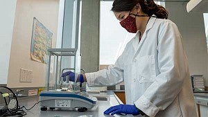 A female student working in a lab wearing a mask, gloves, and a white coat
