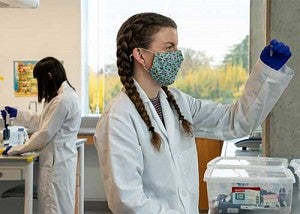 Two students working in a lab wearing masks, coats, and gloves.