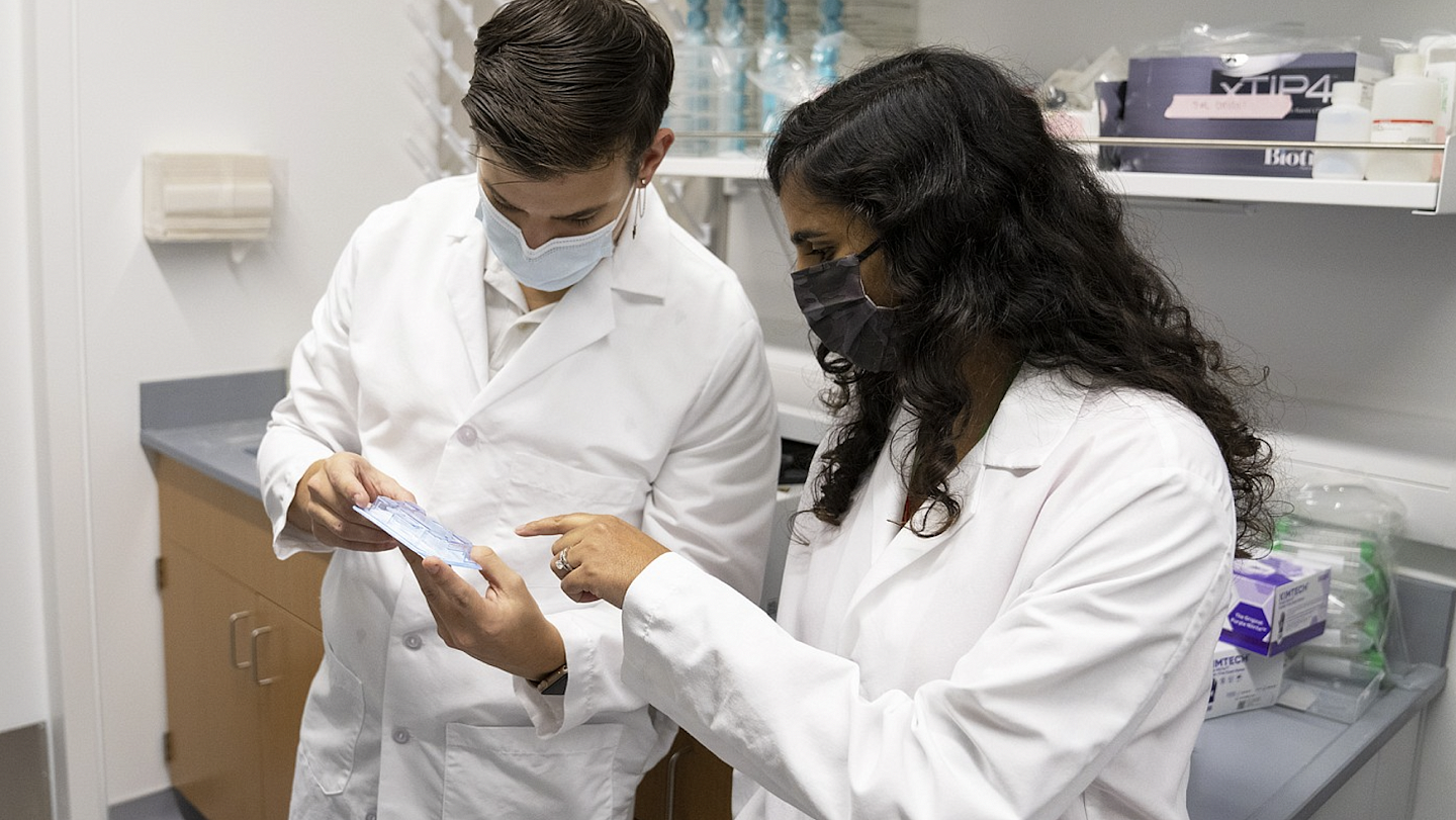 A man and woman in white lab coats look at a medical device
