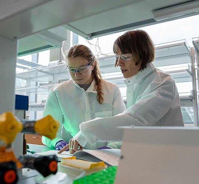 two people wearing white coats and safety goggles in a lab