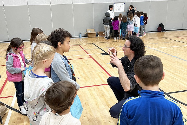 A person kneels with a group of kids in a gym