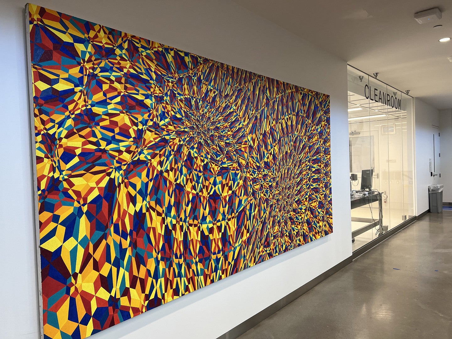 A very large modern painting covering nearly a whole wall that has lots of intricate shapes filled with different colors