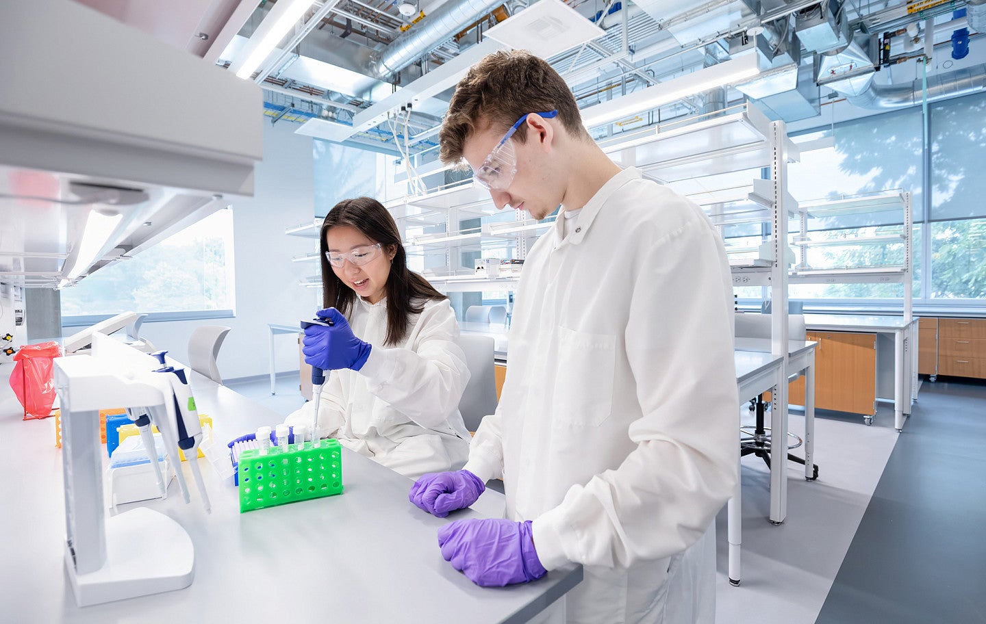 Young woman in lab coat with pipette and young man in lab coat beside her 