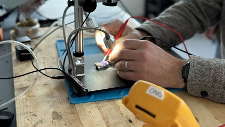 Close-up of two hands soldering electronic device