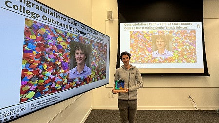 A man holds an award next to two large screens with his photo