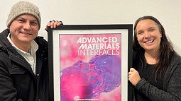 Chakris Kussalanant and Gabby Lindberg stand next to print of cover image from science paper