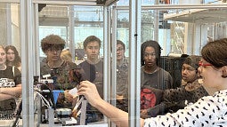 A woman demonstrates how to use a large 3D printer for a group of high school students