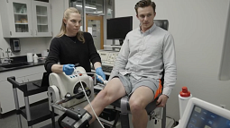 Human physiology researcher stands alongside research subject doing leg extensions