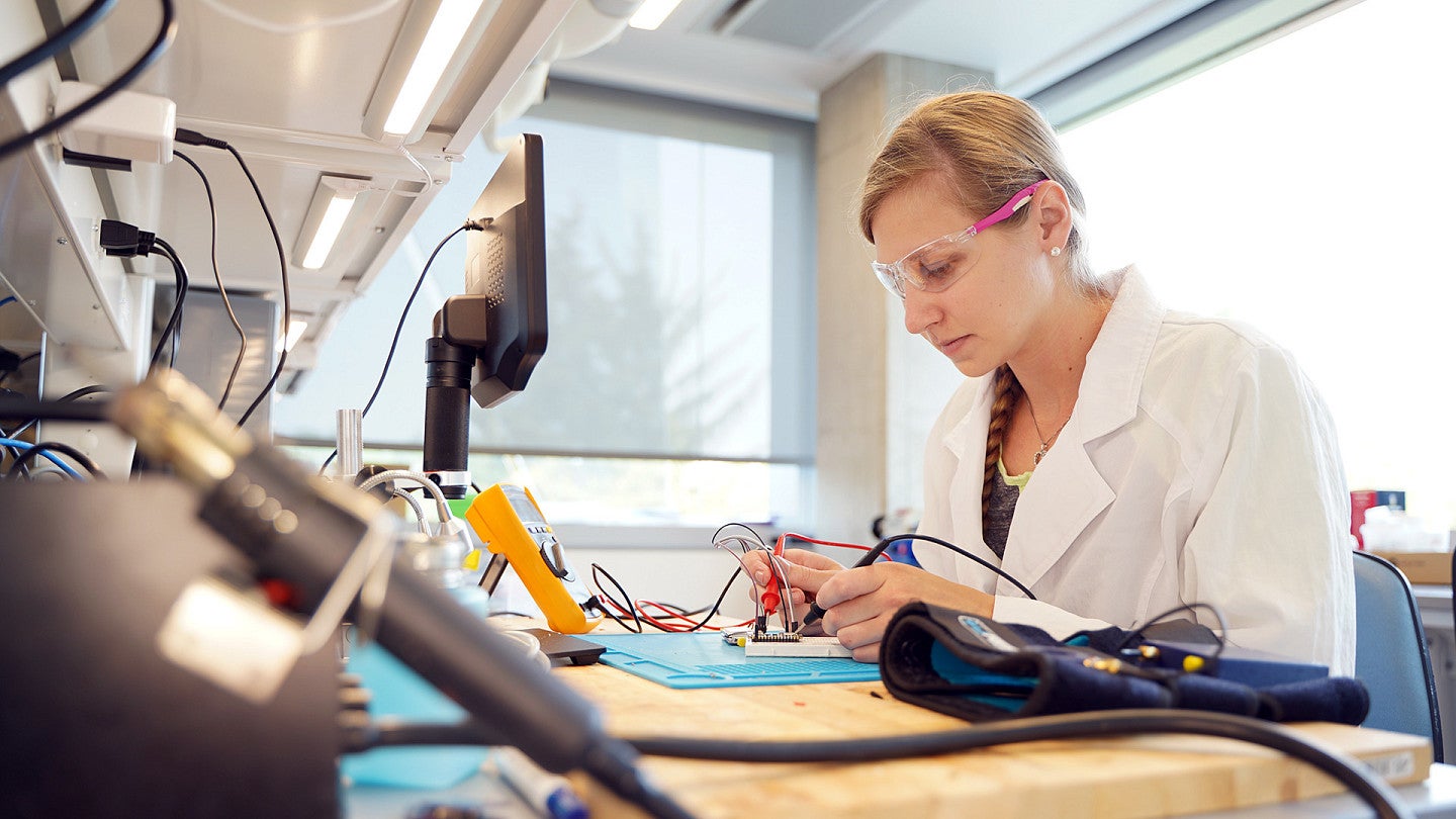A woman in a white lab coat works with electronics