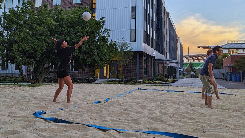 Woman serving volleyball on sand court with teamates to her right