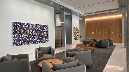Two large modern paintings hang on two walls. There is a large sitting area with chairs and tables and doors leading to other rooms.