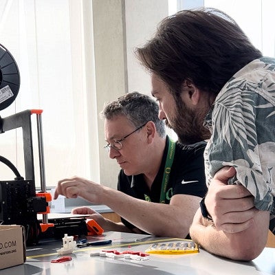 Two men in a lab tinkering with 3-d printer